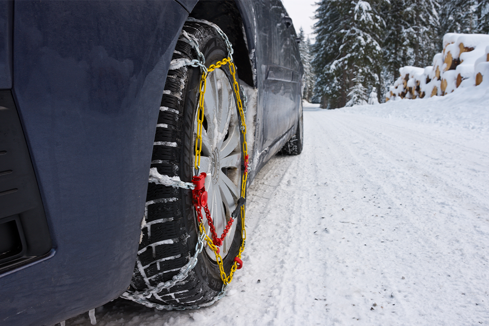 Tire Chains Close up of tire chains on the rear right wheel of a caar driving on a snow-covered road.