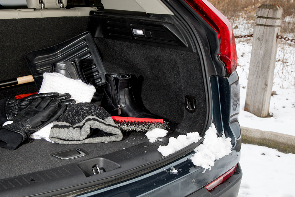 The view inside the open trunk of a vehicle stocked with winter gear like gloves, jumper cables and a snow shovel.