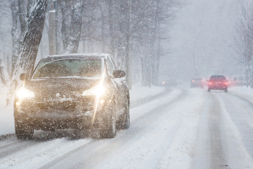 A truck drives through snowy weather with its headlights on